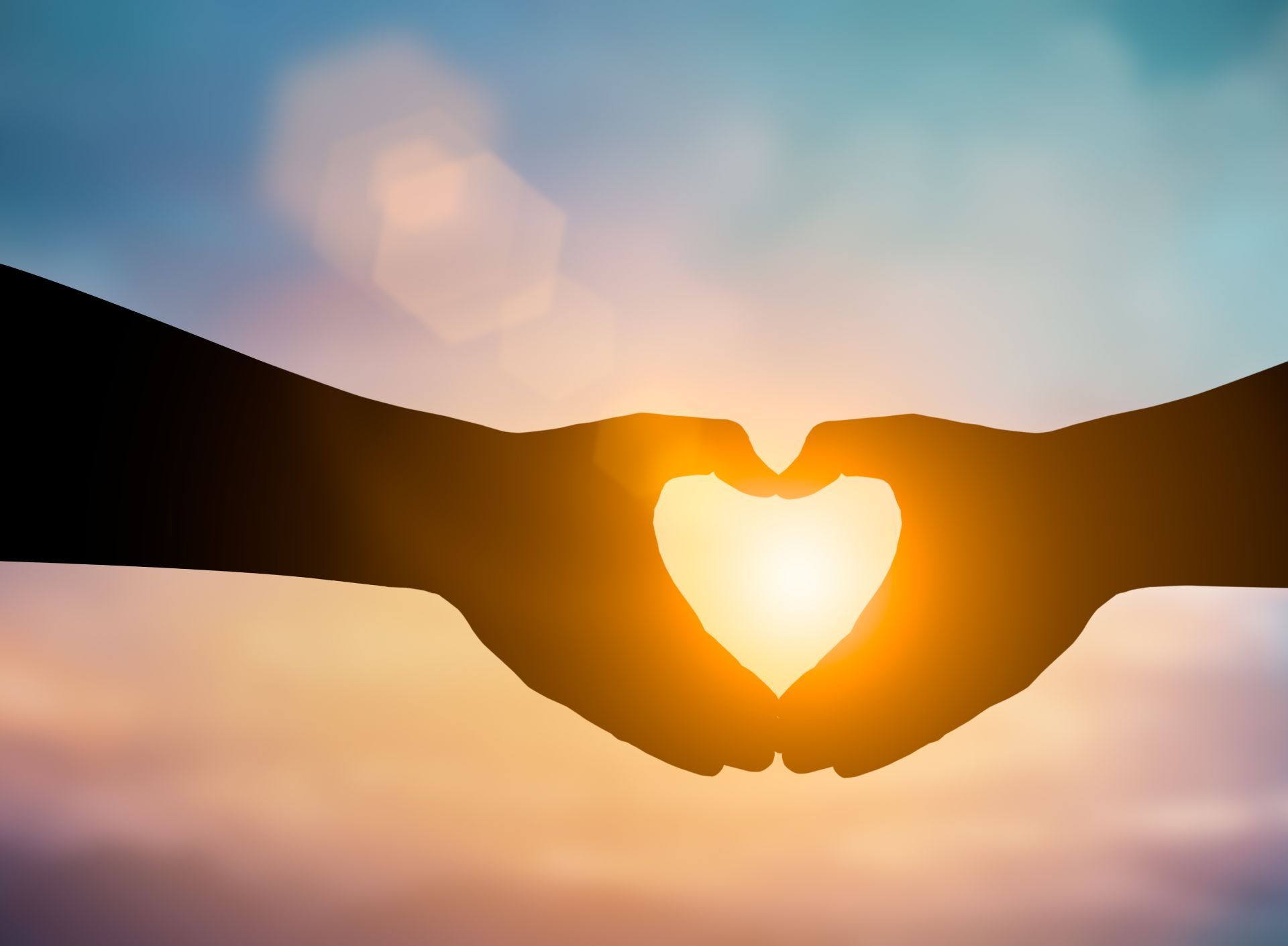Silhouette of hands forming a heart shape, with the sun shining brightly within.