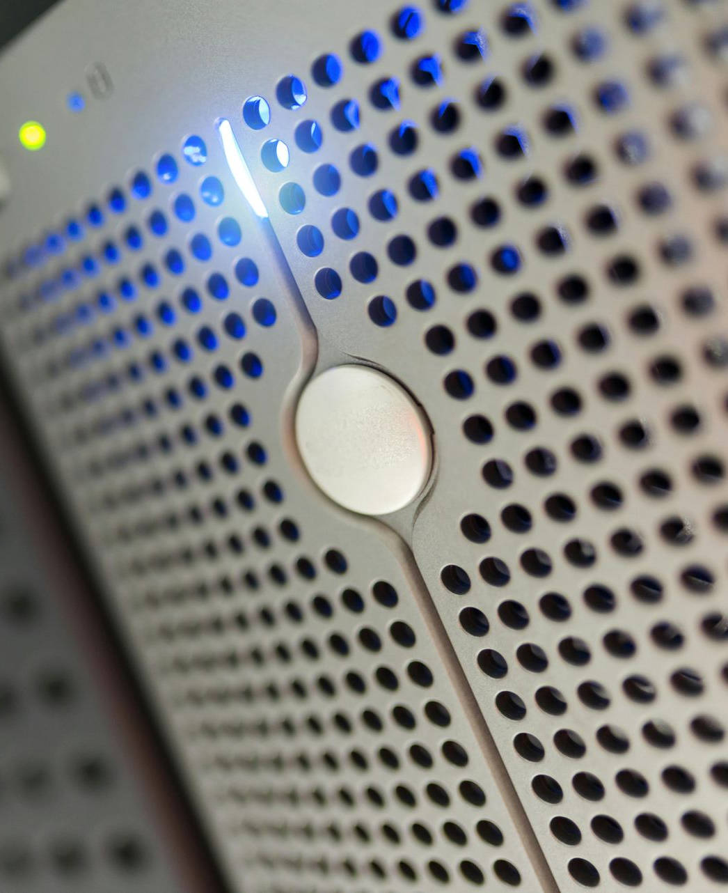 Silver server with blue and yellow lights, perforated metal panel, and a central button.