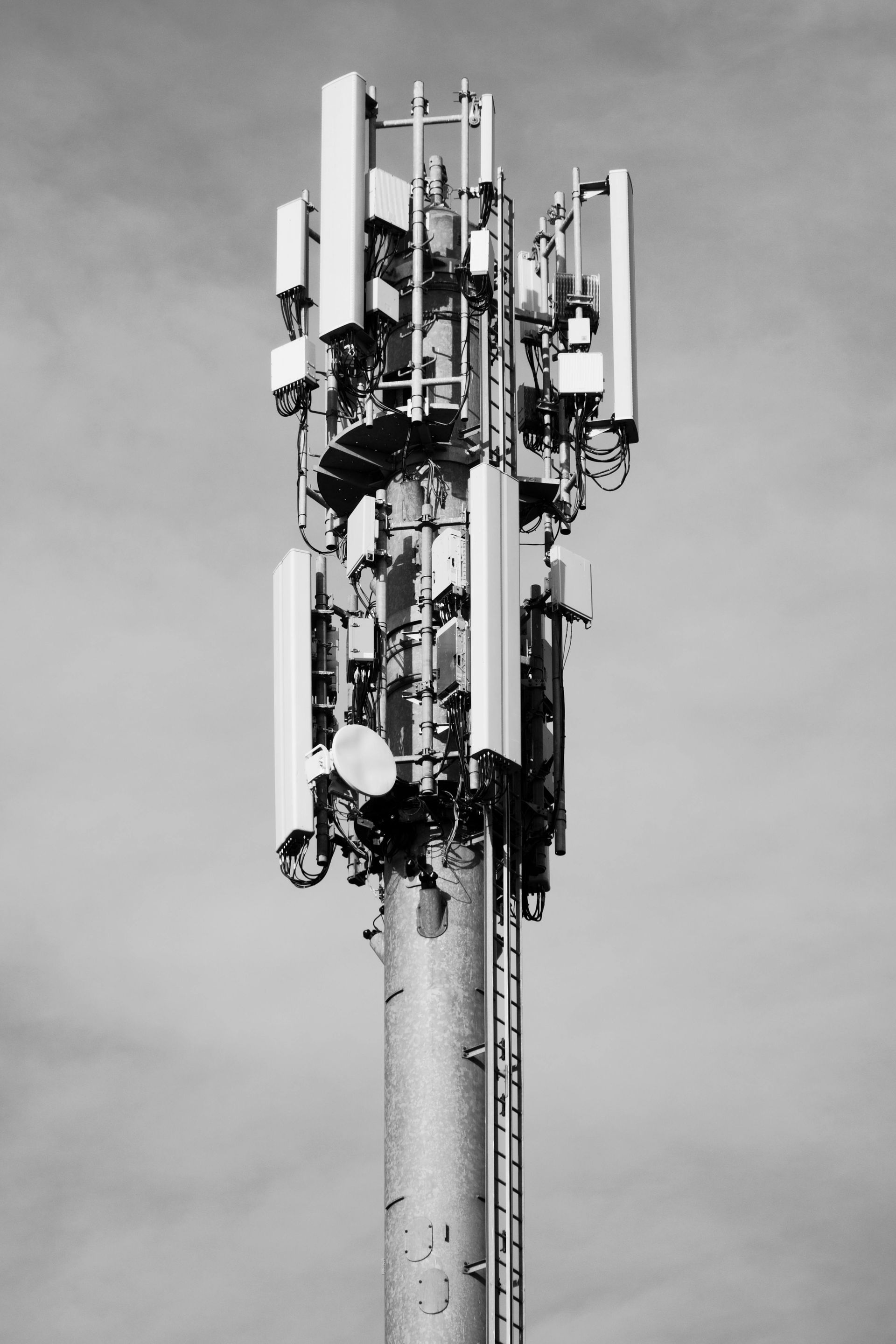 Cell phone tower with multiple antennas against a cloudy sky.