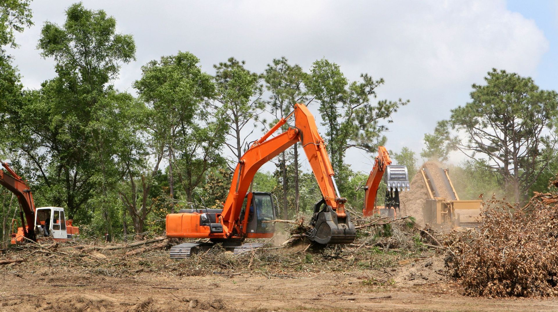 Excavator clearing fallen trees, brush, and outdoor debris from a large property during a tree service