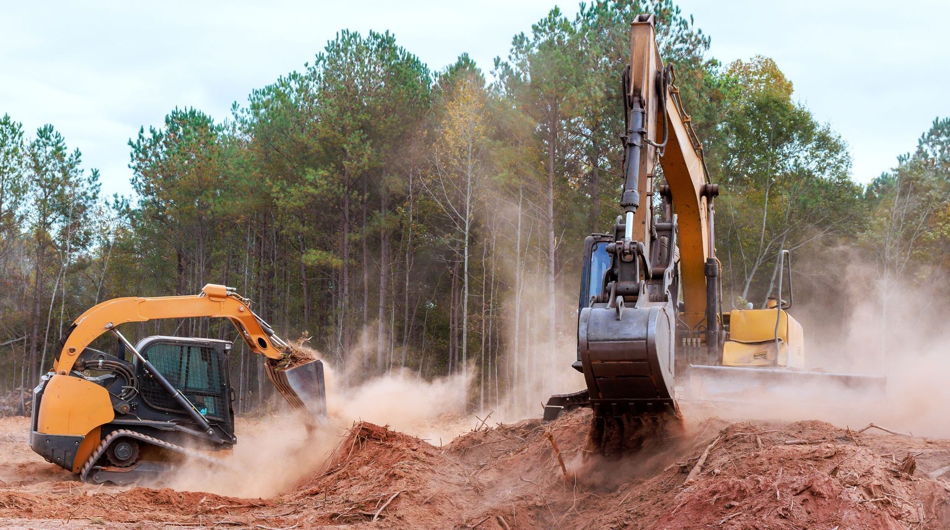 Excavator clearing heavy soil and tree debris from an outdoor job site during a tree service