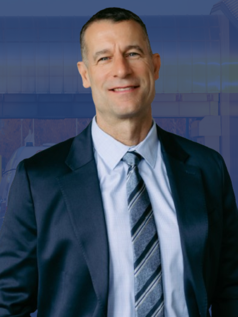 Man in a dark suit and striped tie smiling against a blue studio background