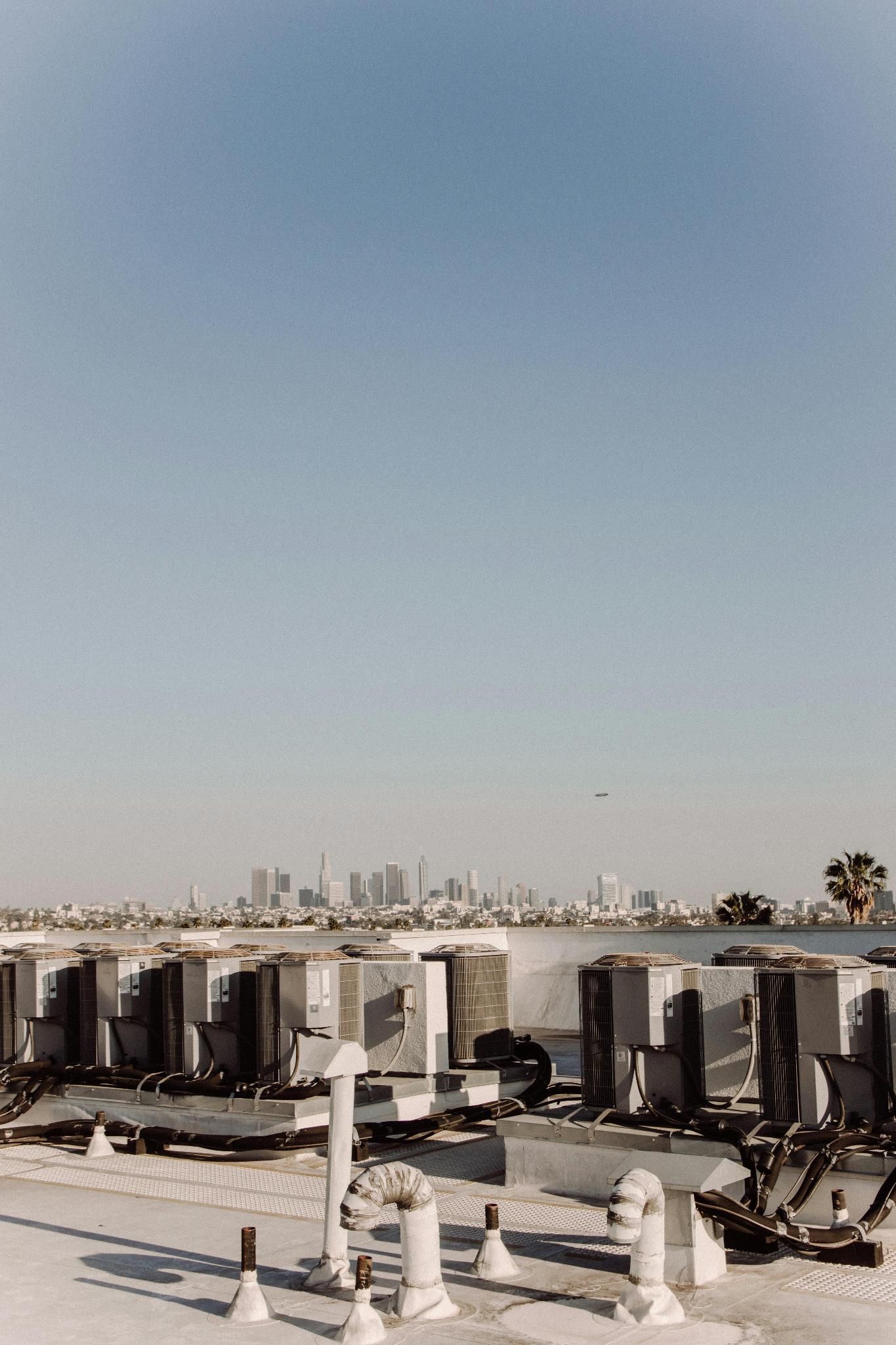 Rooftop HVAC units facing a distant city skyline under a clear blue sky.