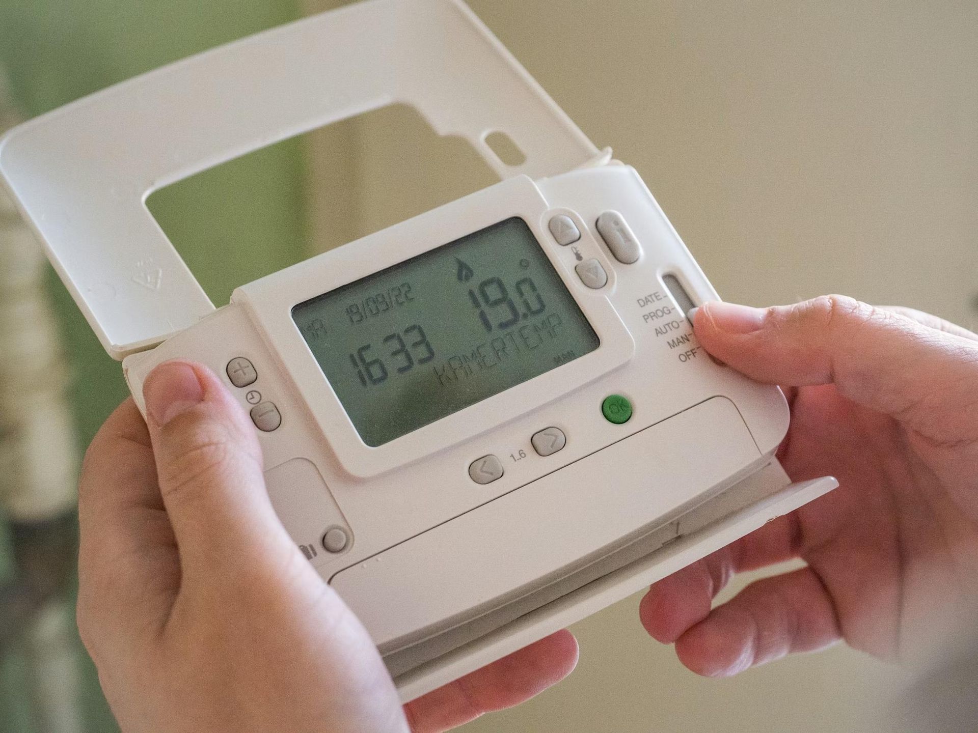 hands adjusting programmable thermostat to improve energy efficiency at home