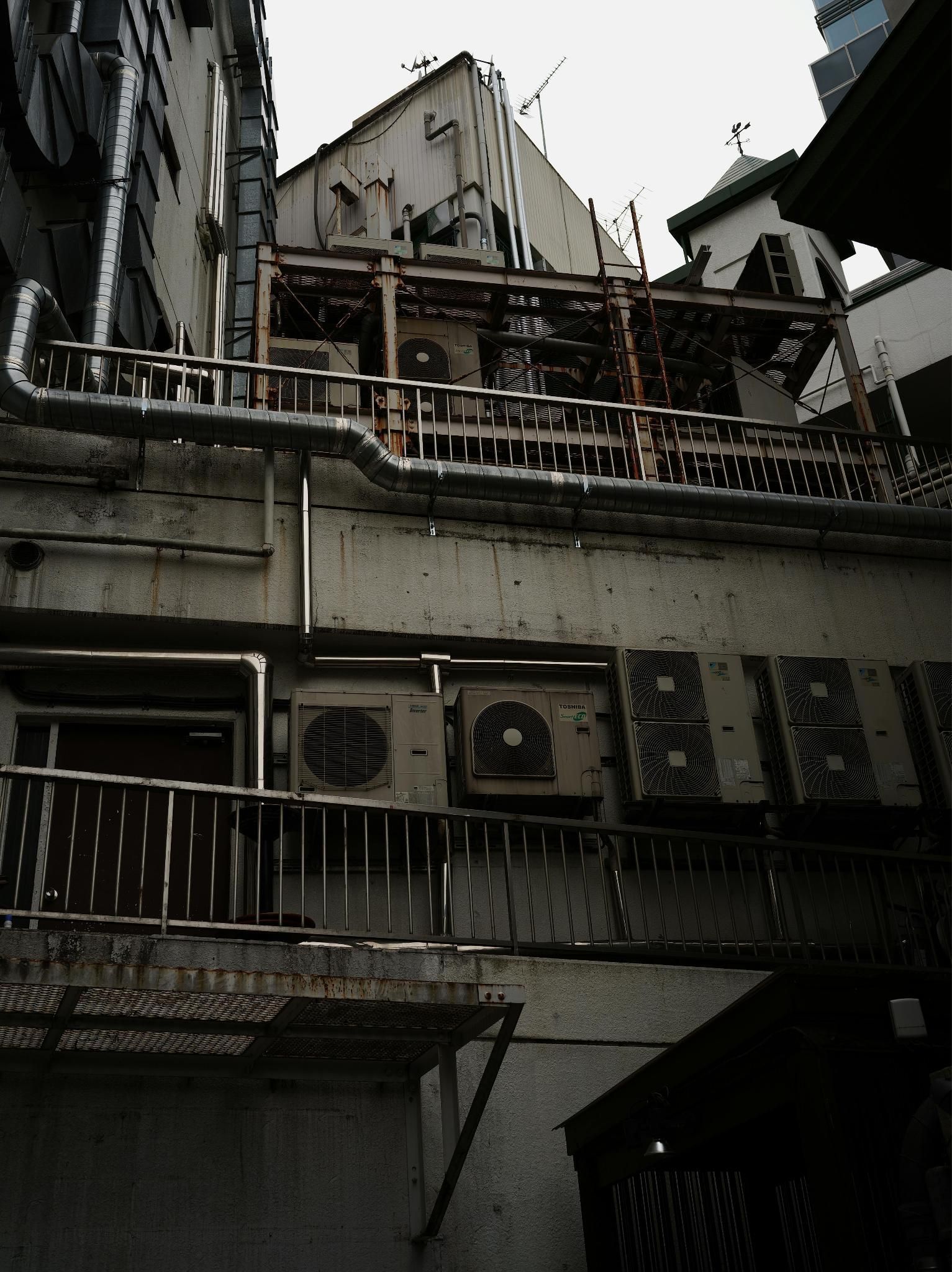 Low angle view of HVAC units on a building wall under urban architecture.
