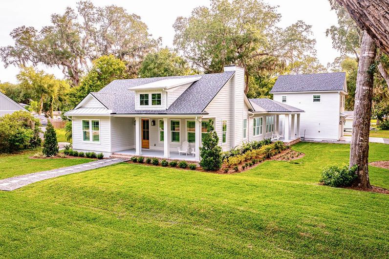 A white house with a large porch is sitting on top of a lush green lawn.