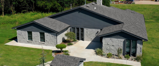 An aerial view of a large house with a gray roof surrounded by grass and trees.
