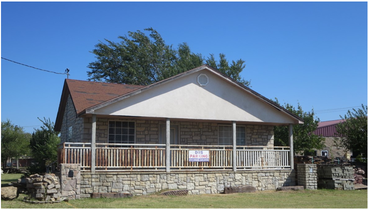 Small white house with a front porch, stone foundation, and red roof on a sunny day