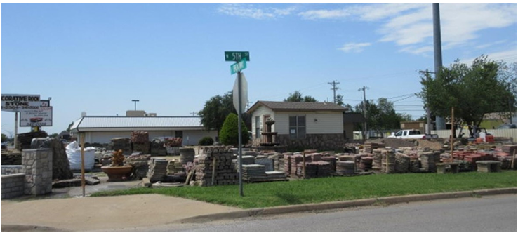 Outdoor stone and brick yard display beside a road, with stacked landscaping materials and a small office building.