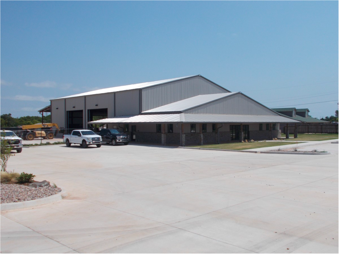 Building with metal roof and attached garage, cars parked in front, sunny day.