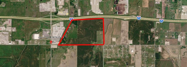 An aerial view of a plot of land outlined in red, positioned between a highway and a road in a rural landscape.