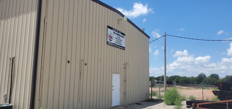 Beige metal warehouse exterior with a white door, sign, and utility lines under a blue sky.