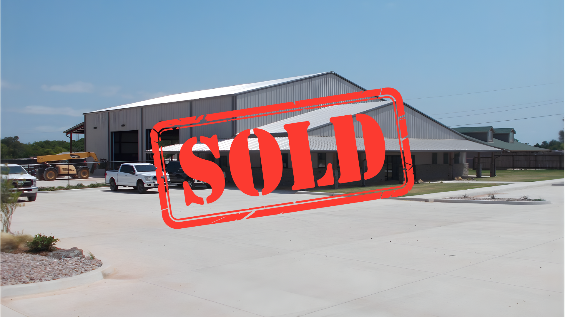 Building with metal roof and attached garage, cars parked in front, sunny day.