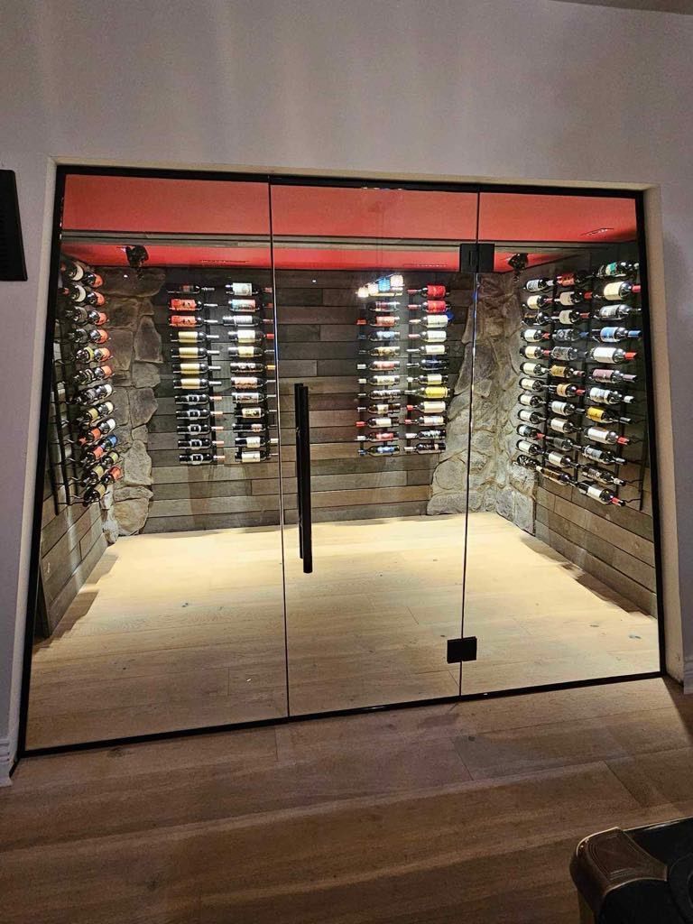 Une cave à vin vitrée avec des étagères murales, un parquet en bois foncé et un éclairage rouge d'ambiance.