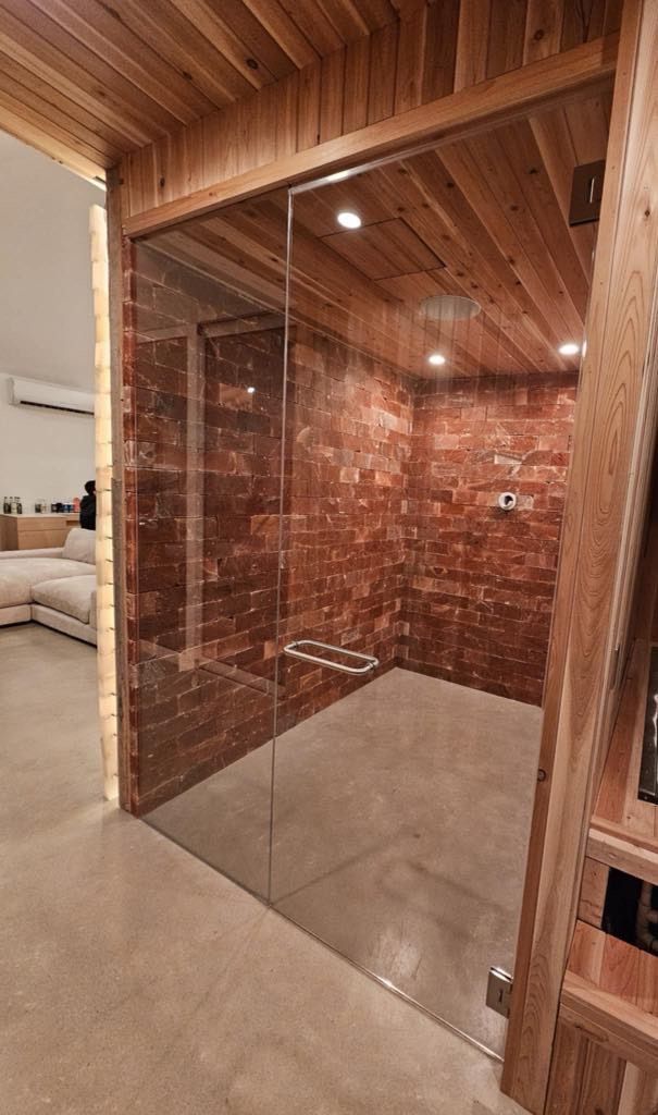 Une salle de bain avec une porte vitrée et un mur en briques.