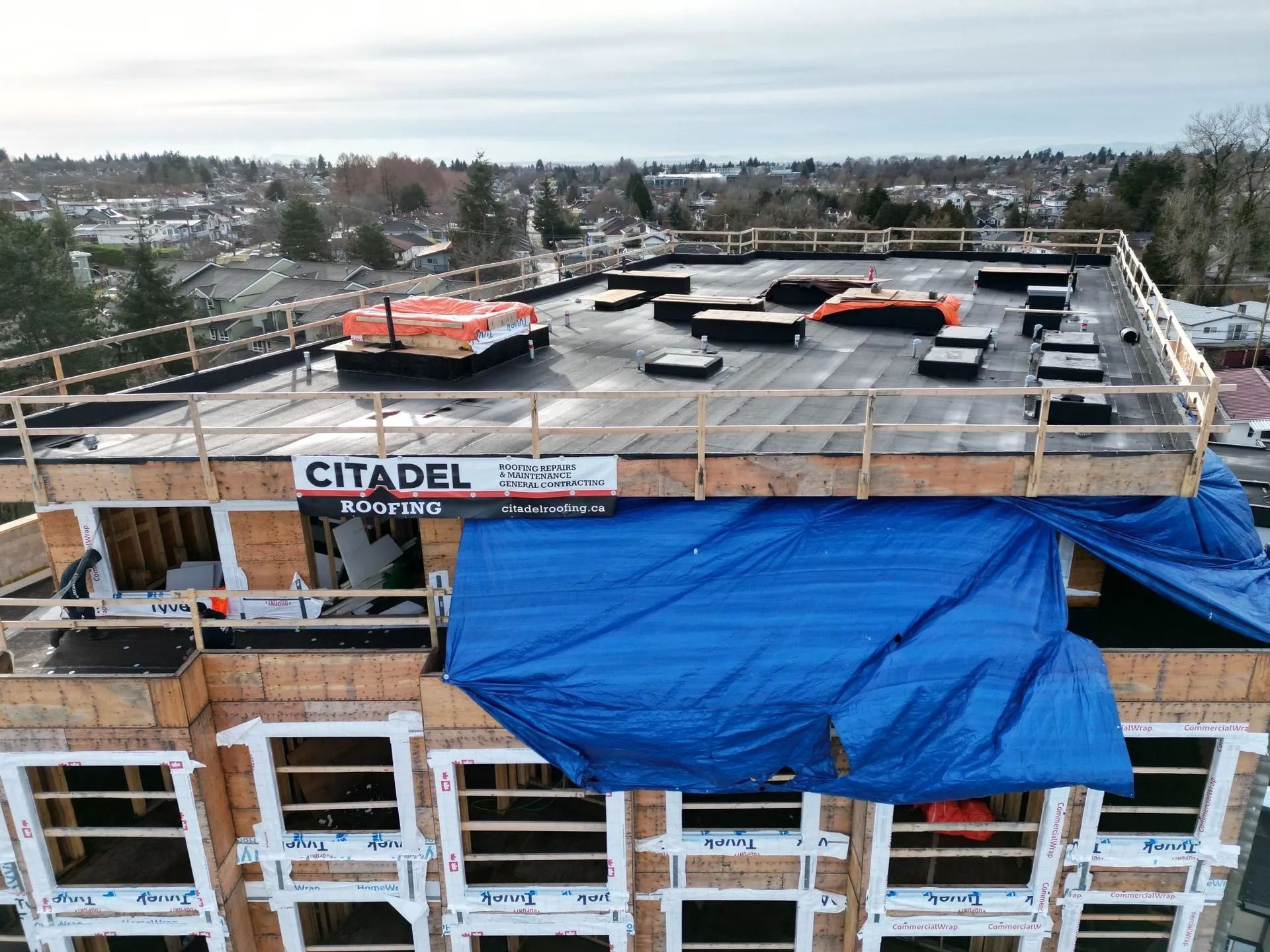 Rooftop construction with blue tarp, orange equipment, and snowy landscape in the background