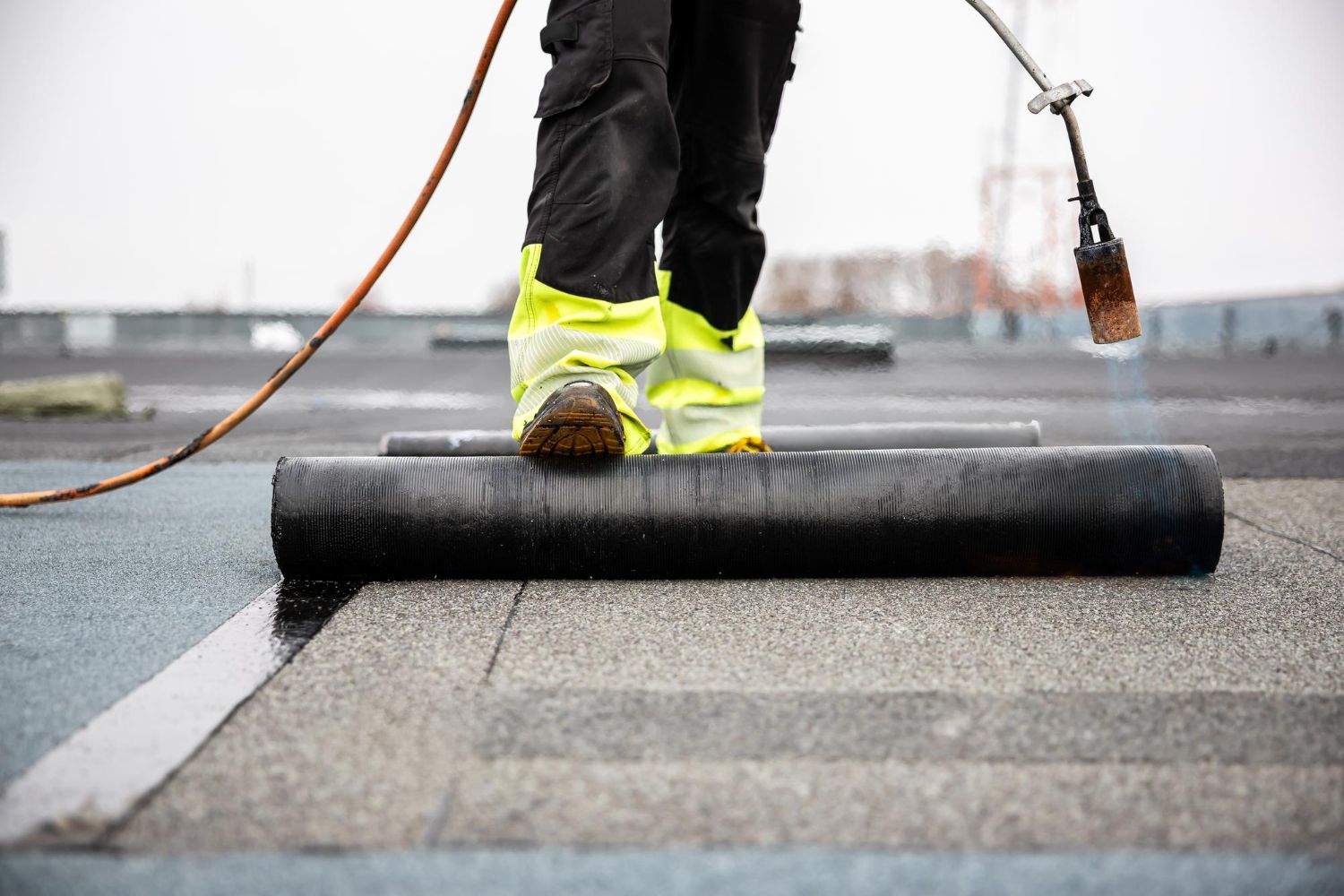 Worker laying black roofing material with a torch on a wet roof