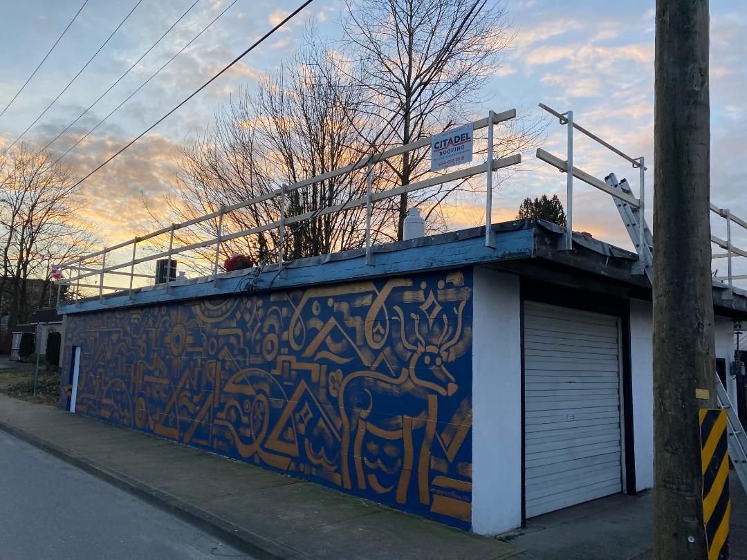 Blue utility building with orange mural, roller door, and bare trees at sunset by a roadside