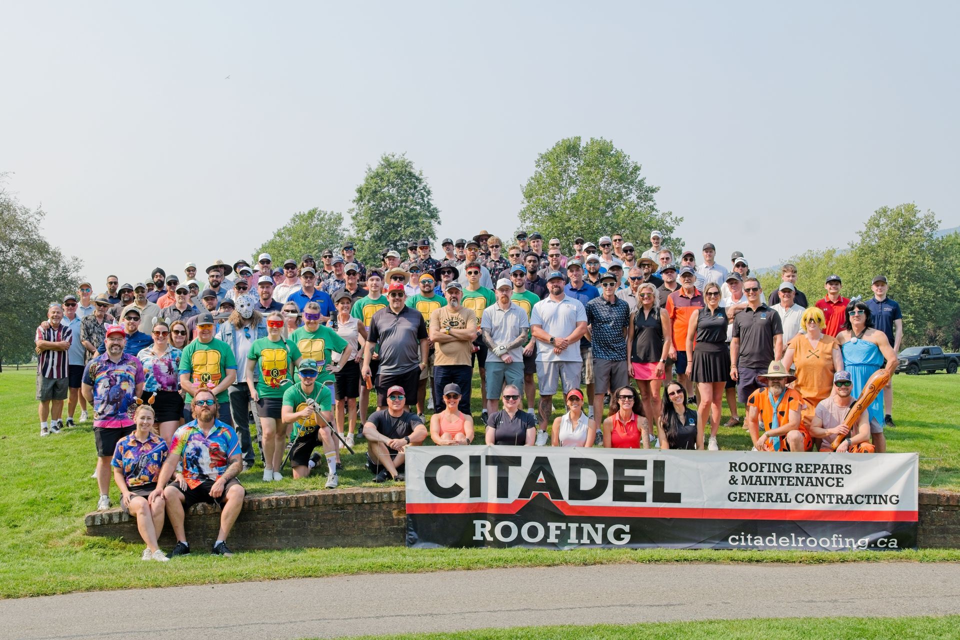 A large group of people are posing for a picture in front of a sign that says citadel roofing.