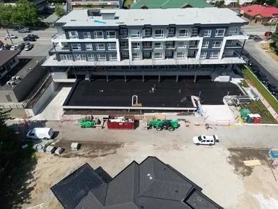 Aerial view of a multi-story building with construction equipment and vehicles in front on a dirt lot