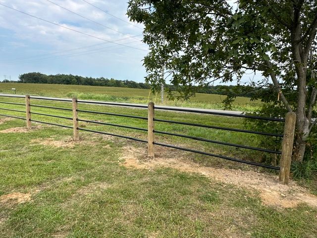 Wooden fence and black rail fence beside a grassy field under a partly cloudy sky