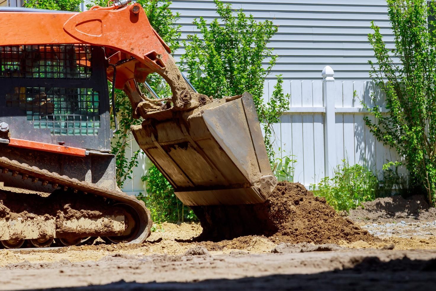 Orange skid-steer loader dumping dirt in a yard beside a gray house