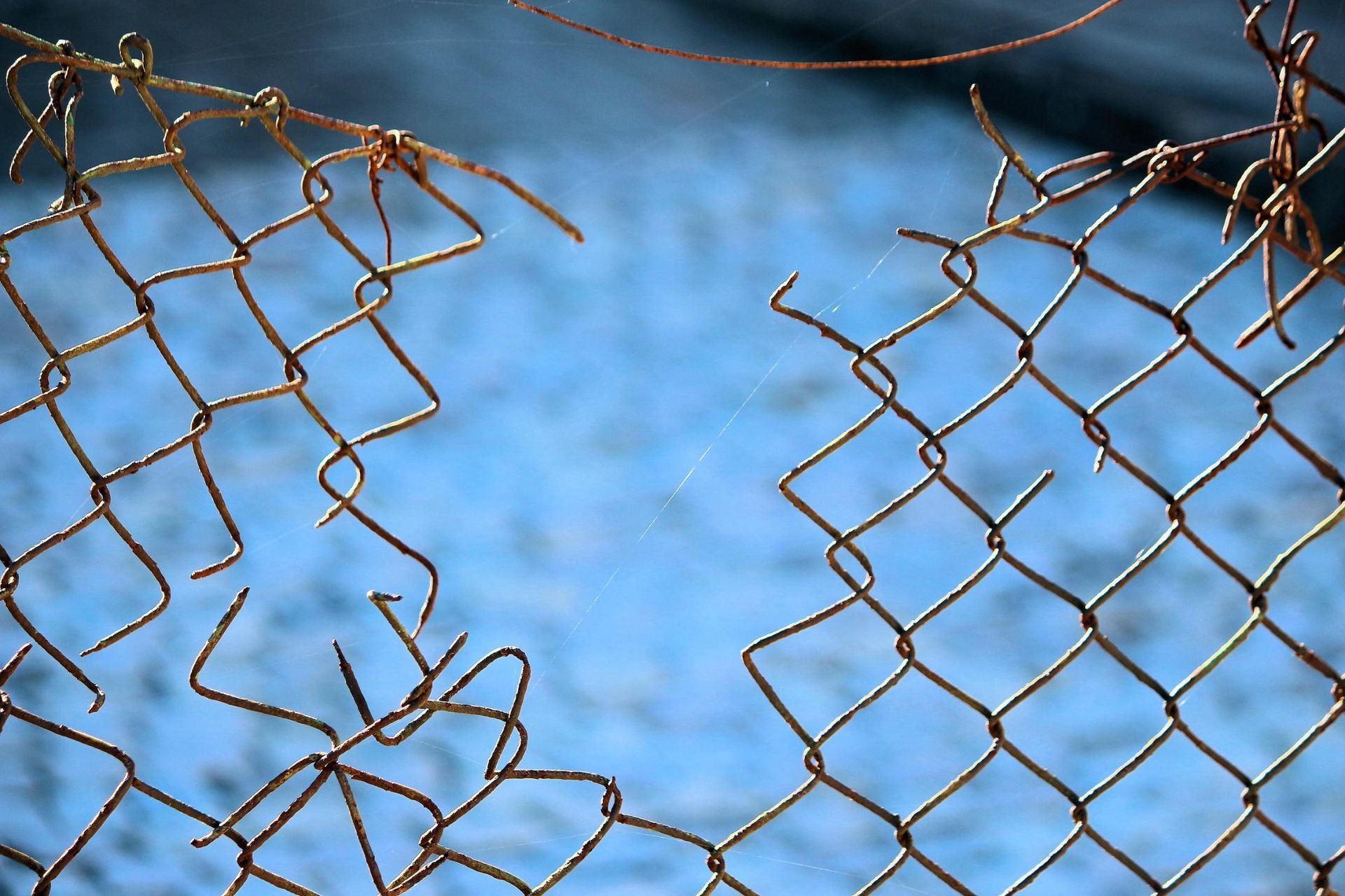 Broken chain-link fence against a blue background