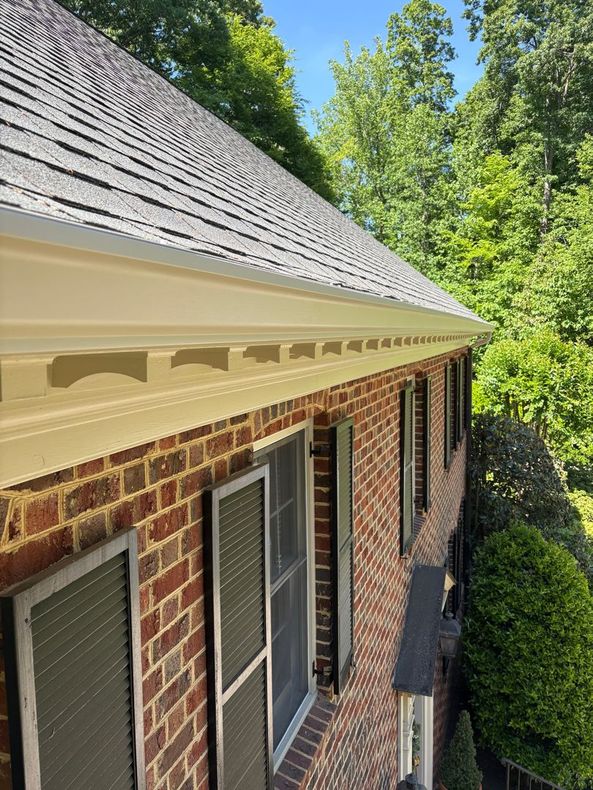 Brick house exterior with white trim, gray shingle roof, and green trees beside it