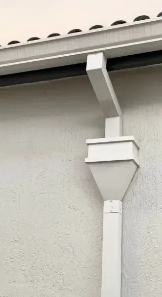 White rain gutter system on a stucco wall.