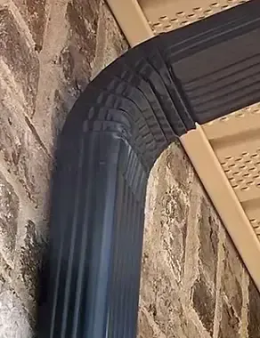 Dark blue gutter making a curved turn, mounted on a brick wall.