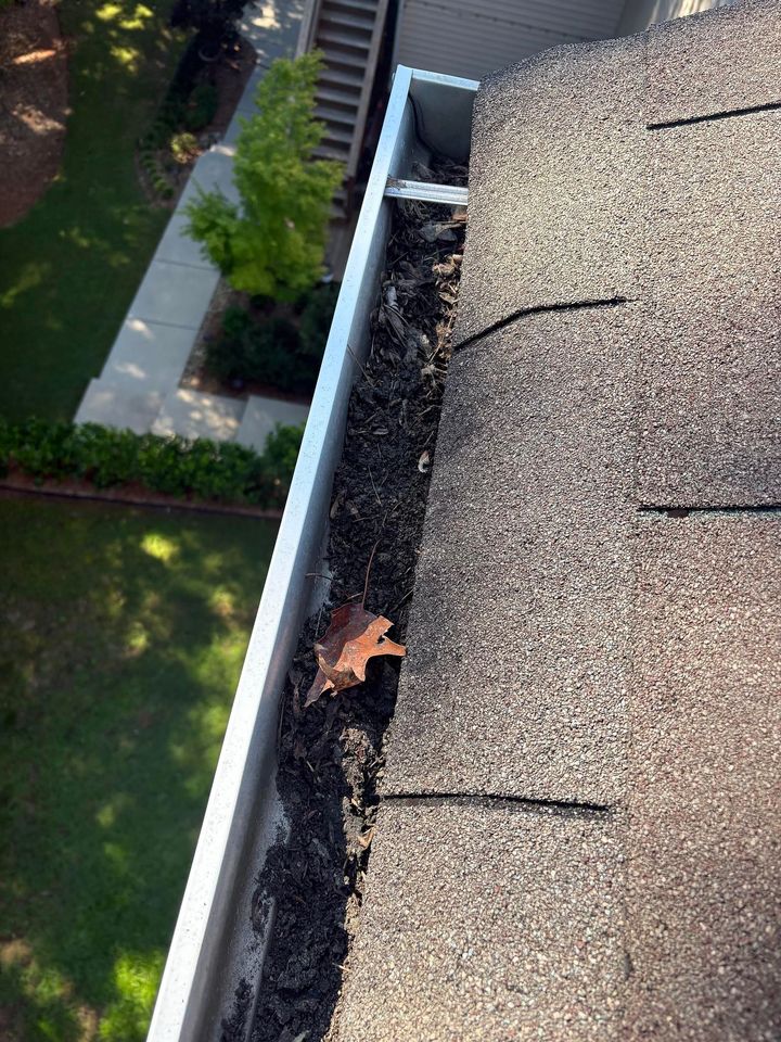 Roof gutter with leaves and debris beside a house, viewed from above