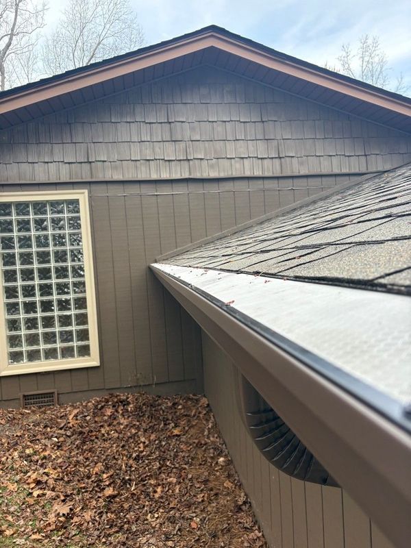 House exterior with brown siding, glass block window, and rain gutter under a shingled roof
