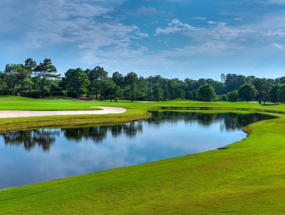 Golf course with a lake reflecting the sky and surrounding greenery.