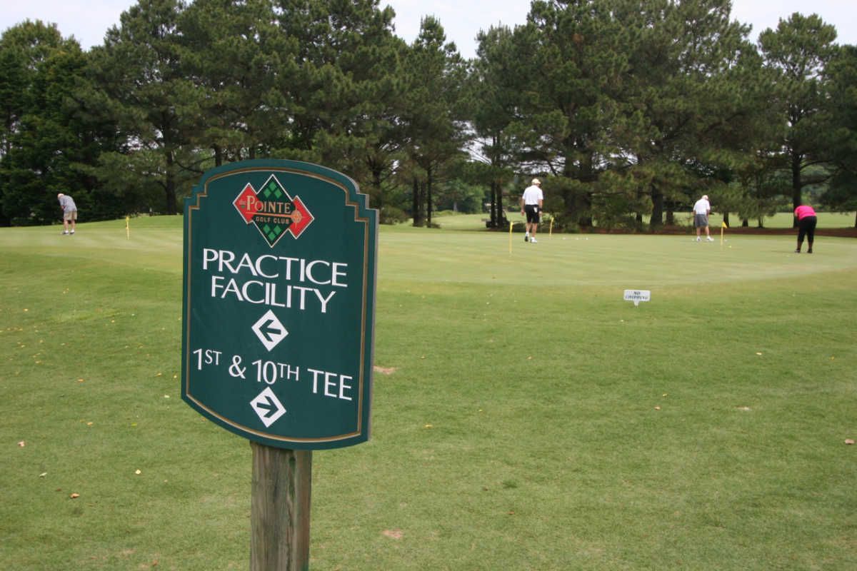 Sign for a practice facility at a golf course with golfers putting in the background.