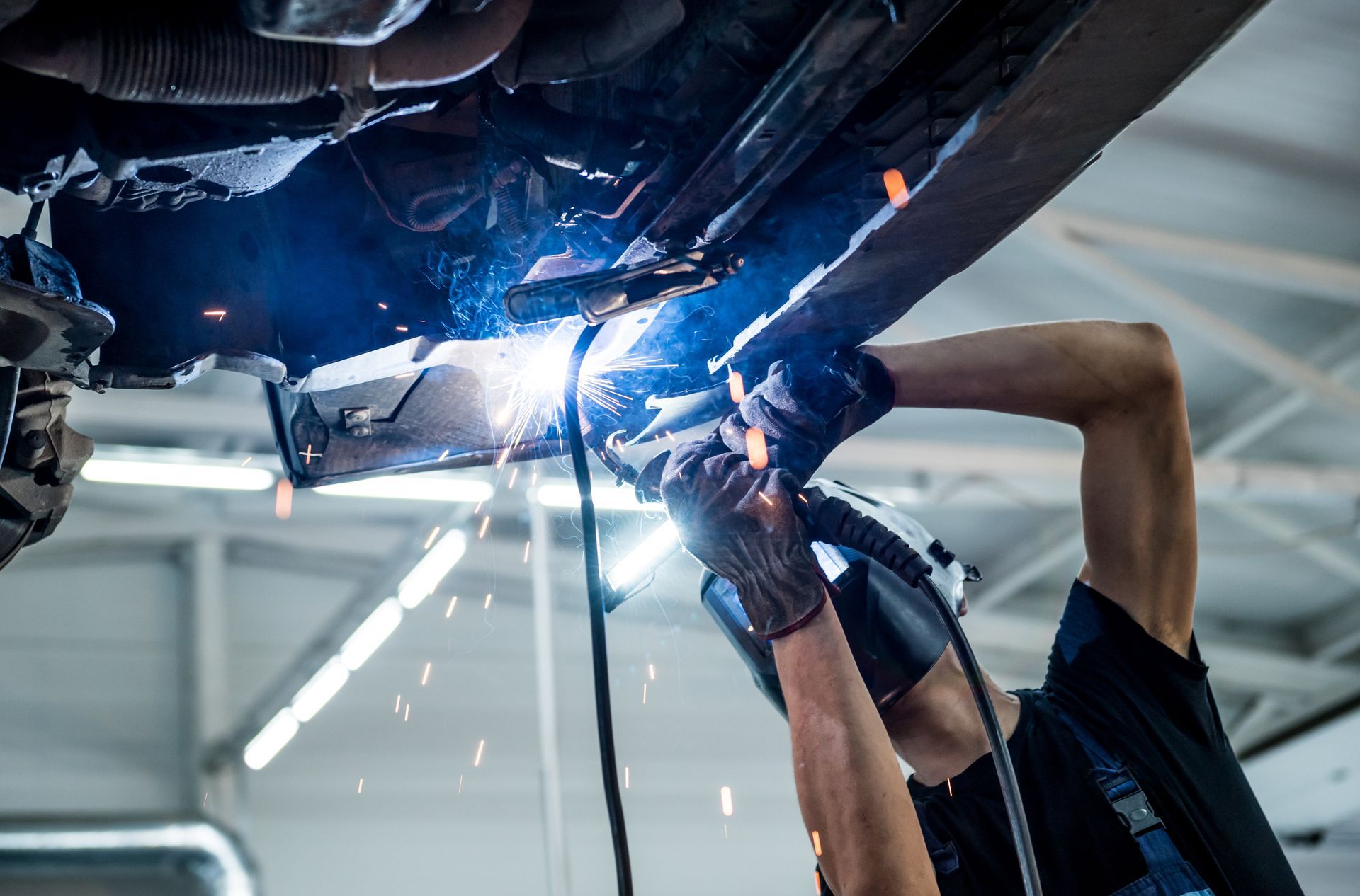 Mechanic welding under a car, bright blue sparks in a garage
