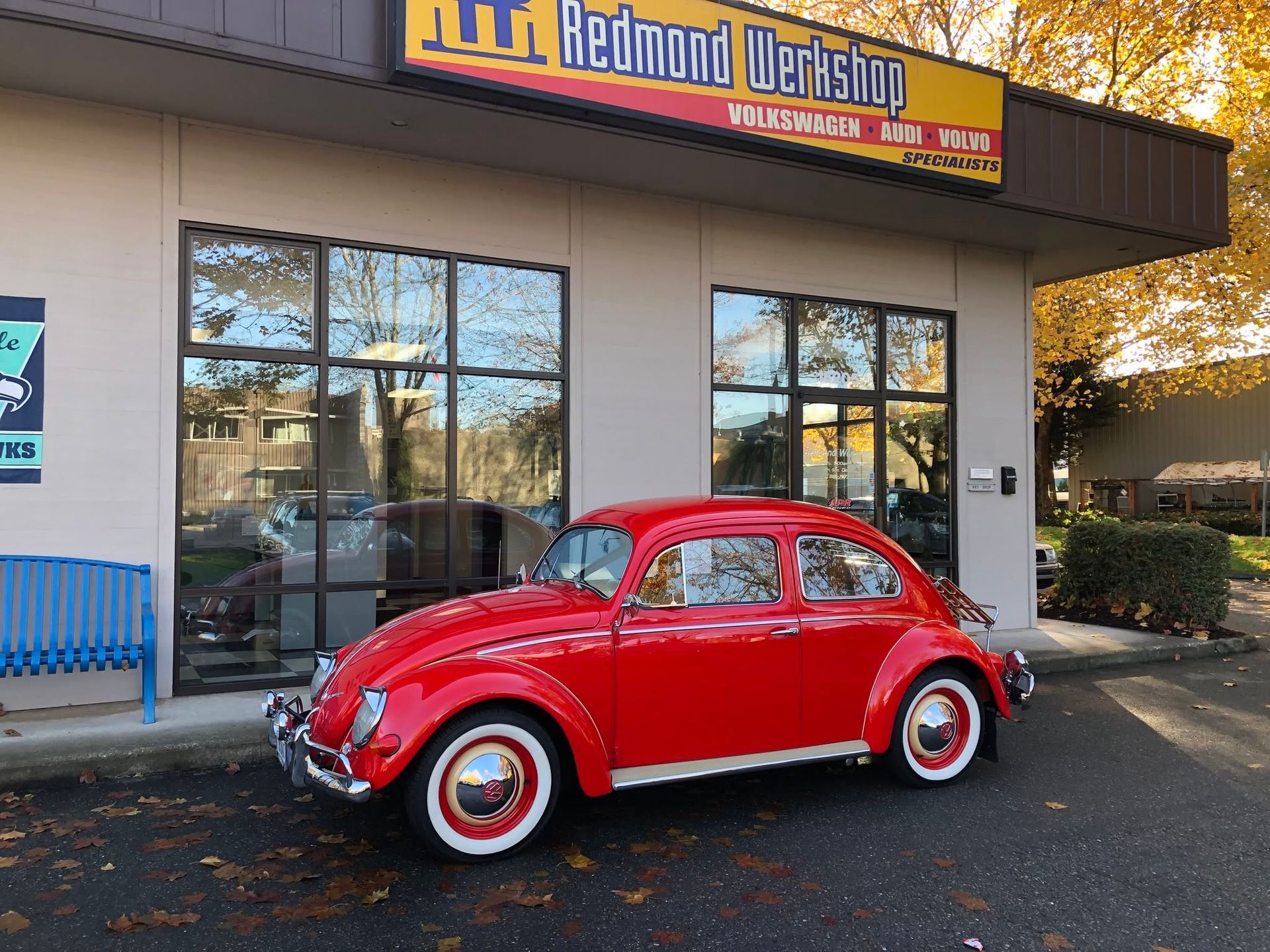 Red classic Volkswagen Beetle parked outside a storefront with glass windows and a workshop sign.