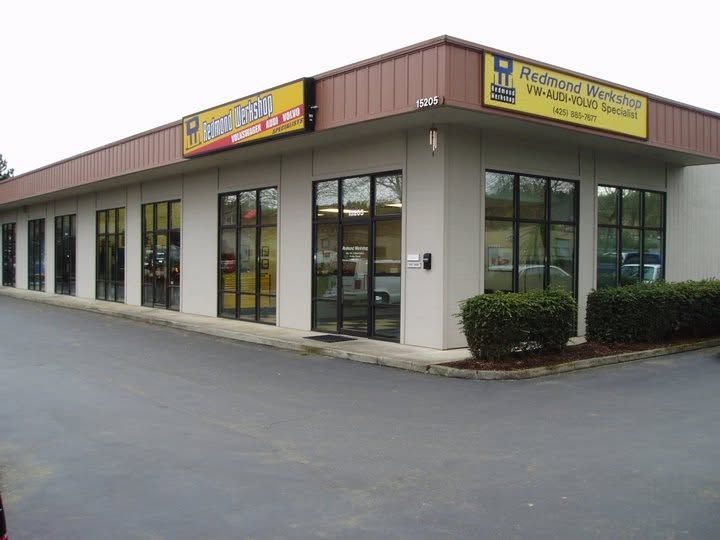 Corner storefront plaza with large windows and yellow signs on a paved lot