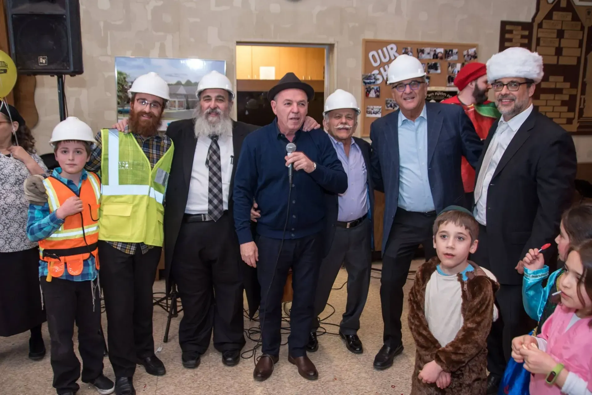 A group of people in hard hats and safety vests standing indoors, with a child in front.