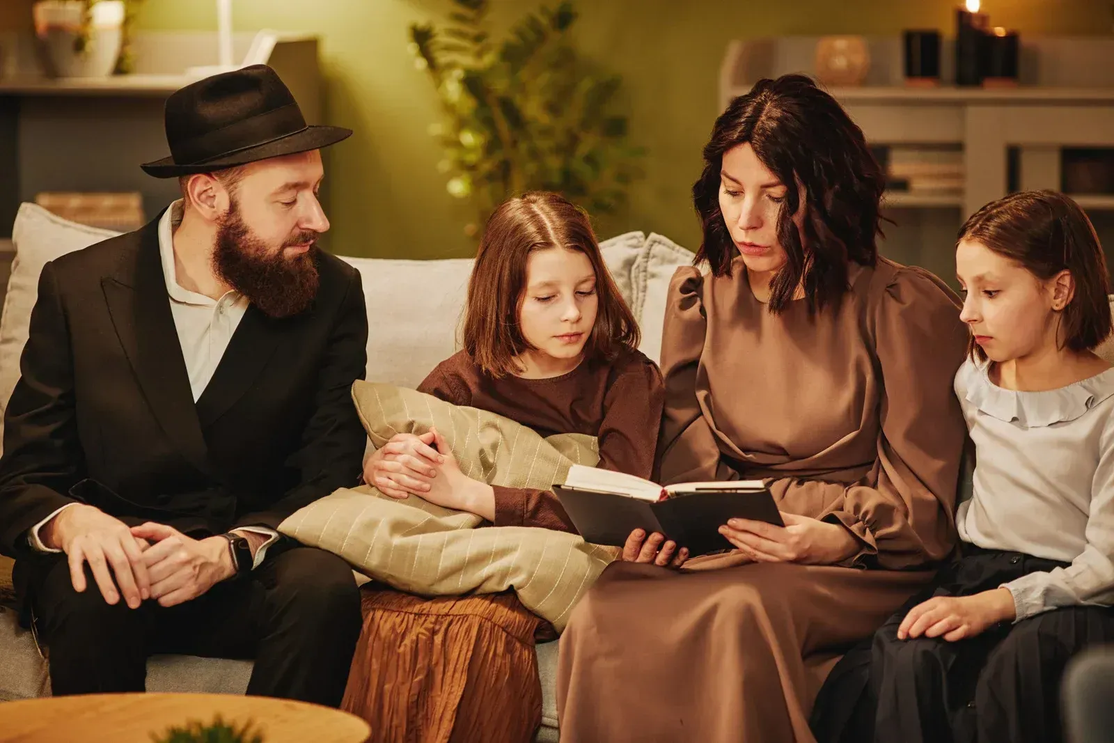 Family reading together on a couch in a cozy, warmly lit living room