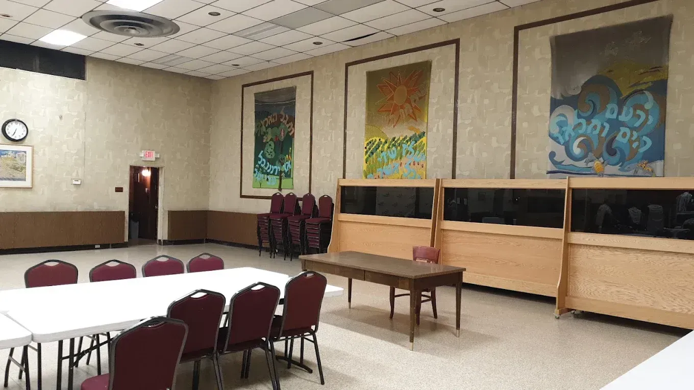 Empty community room with tables, chairs, wall art, and a clock on the left wall.