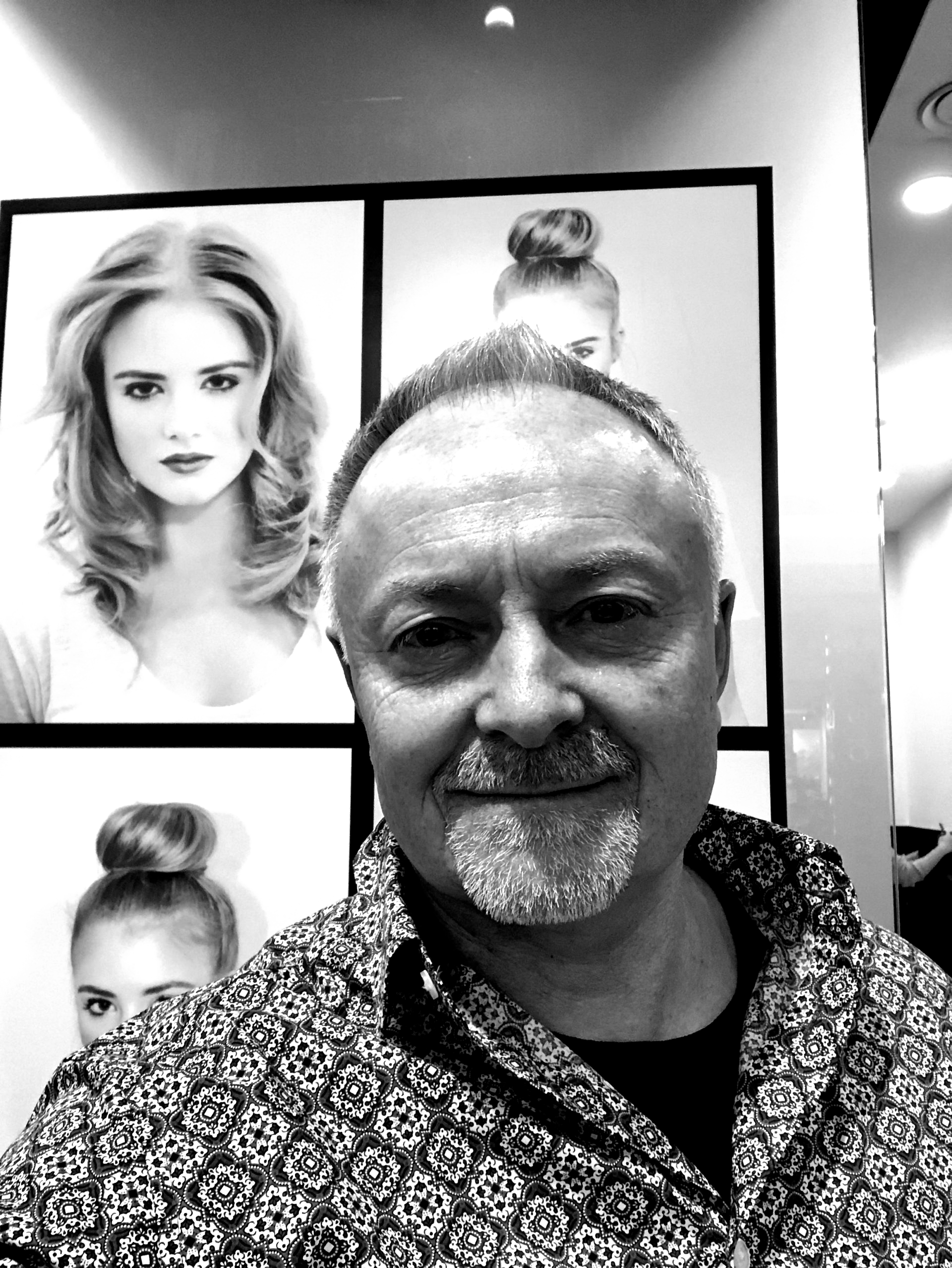 A man with a beard is standing in front of a wall with pictures of women 's hair.