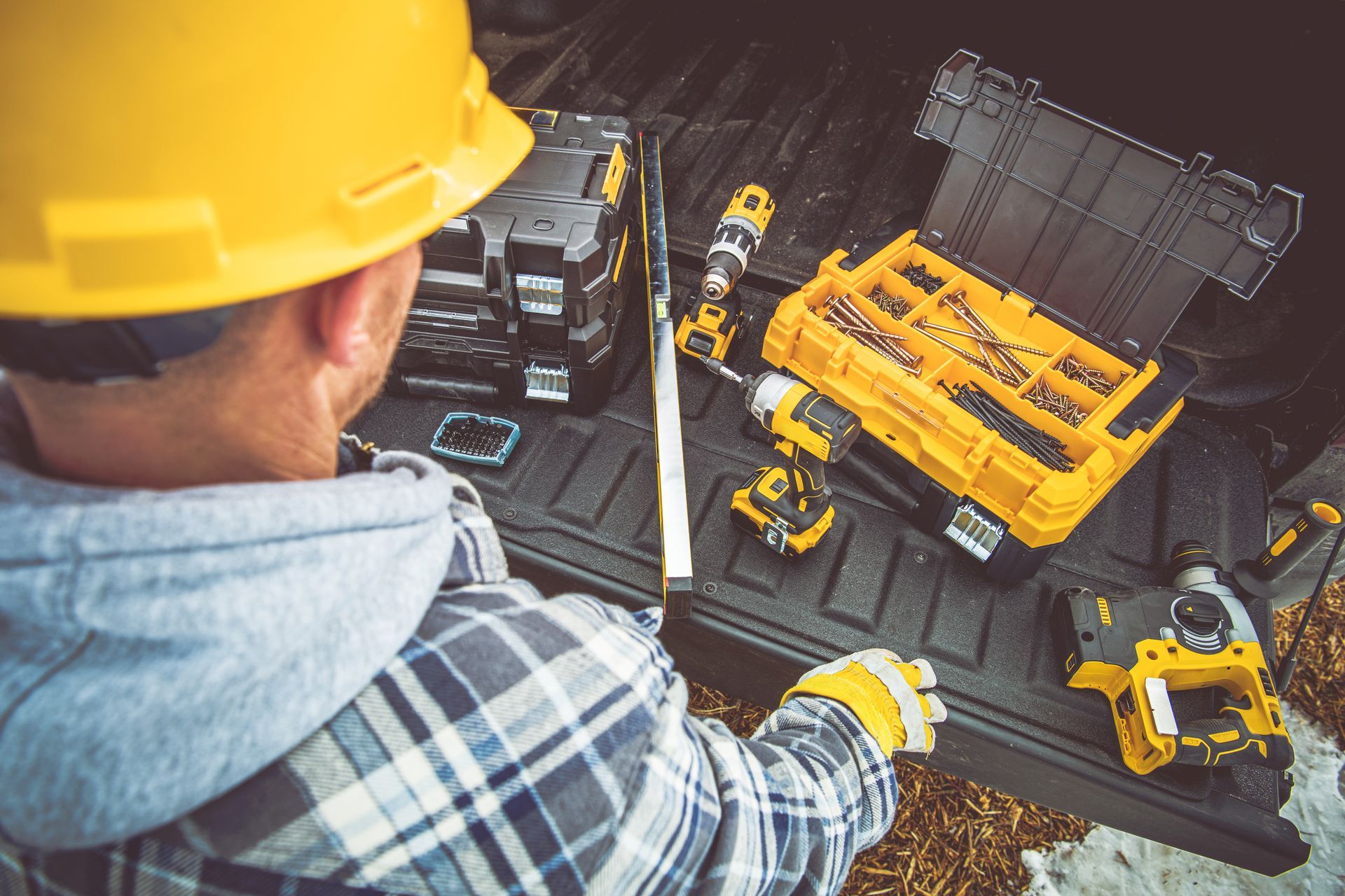 A BACK VIEW OF A BUILDER LOOKING AT TOOLS IN A PICKUP TRUCK.