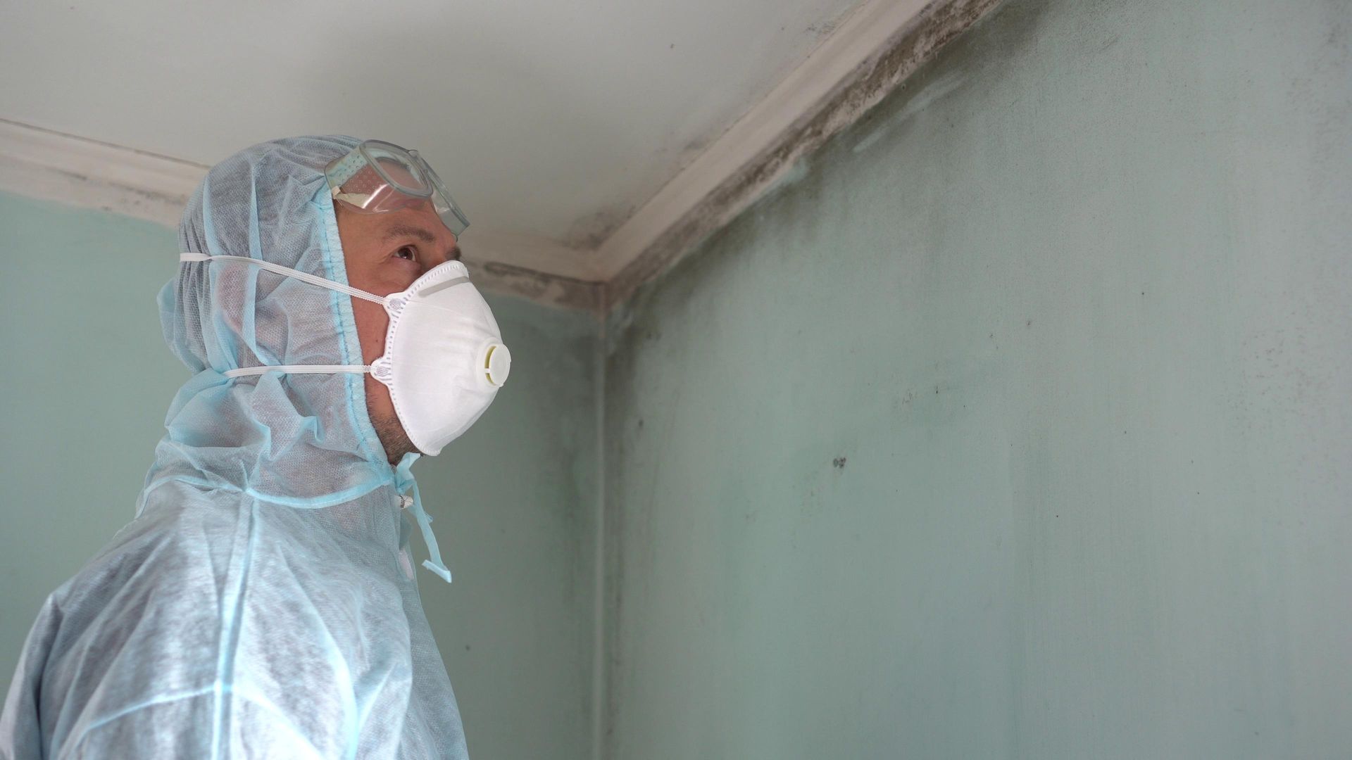 A man wearing a mask and a protective suit is standing in a room.