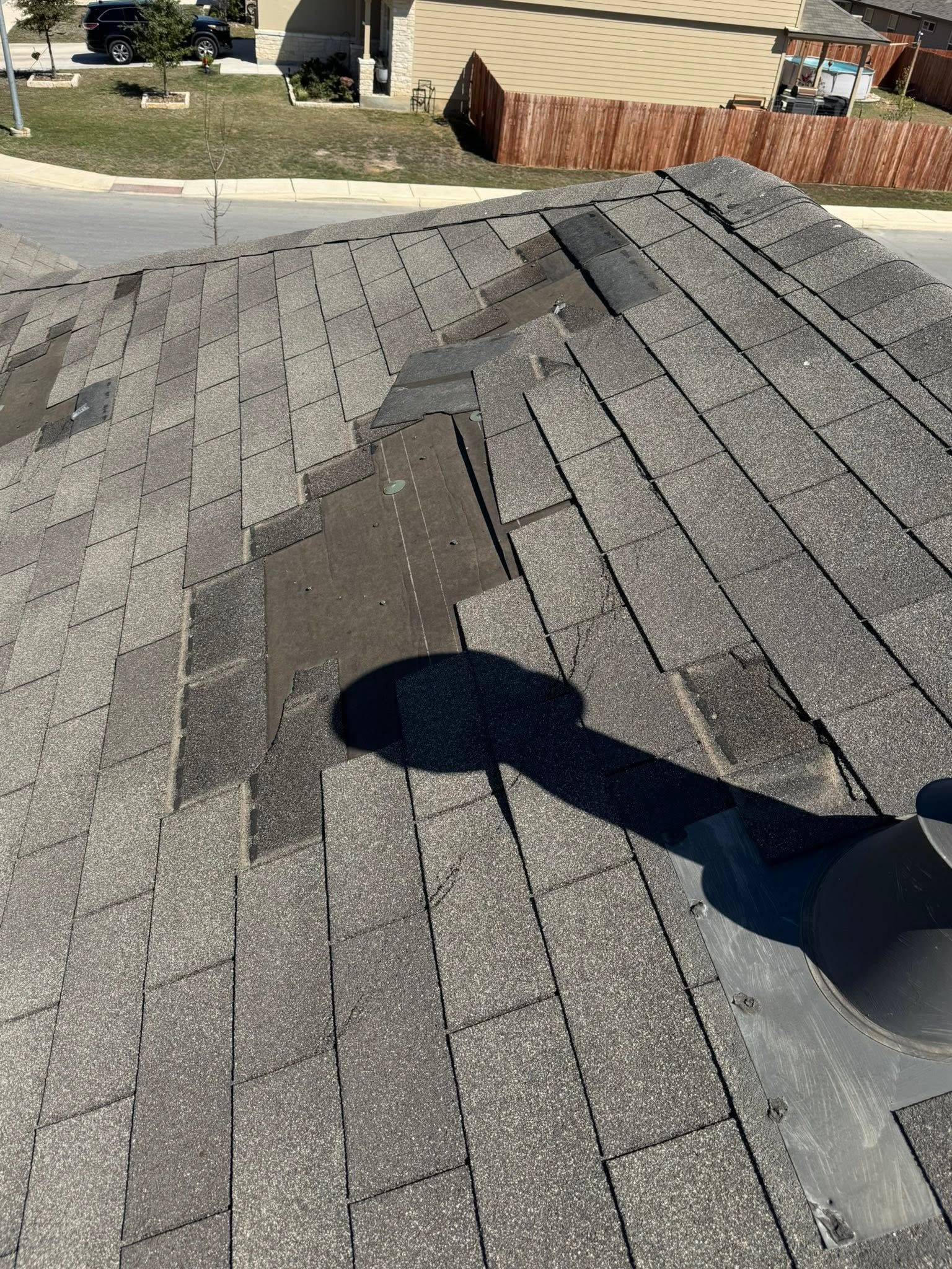 Damaged gray shingle roof with a dark patch and shadows in bright sunlight