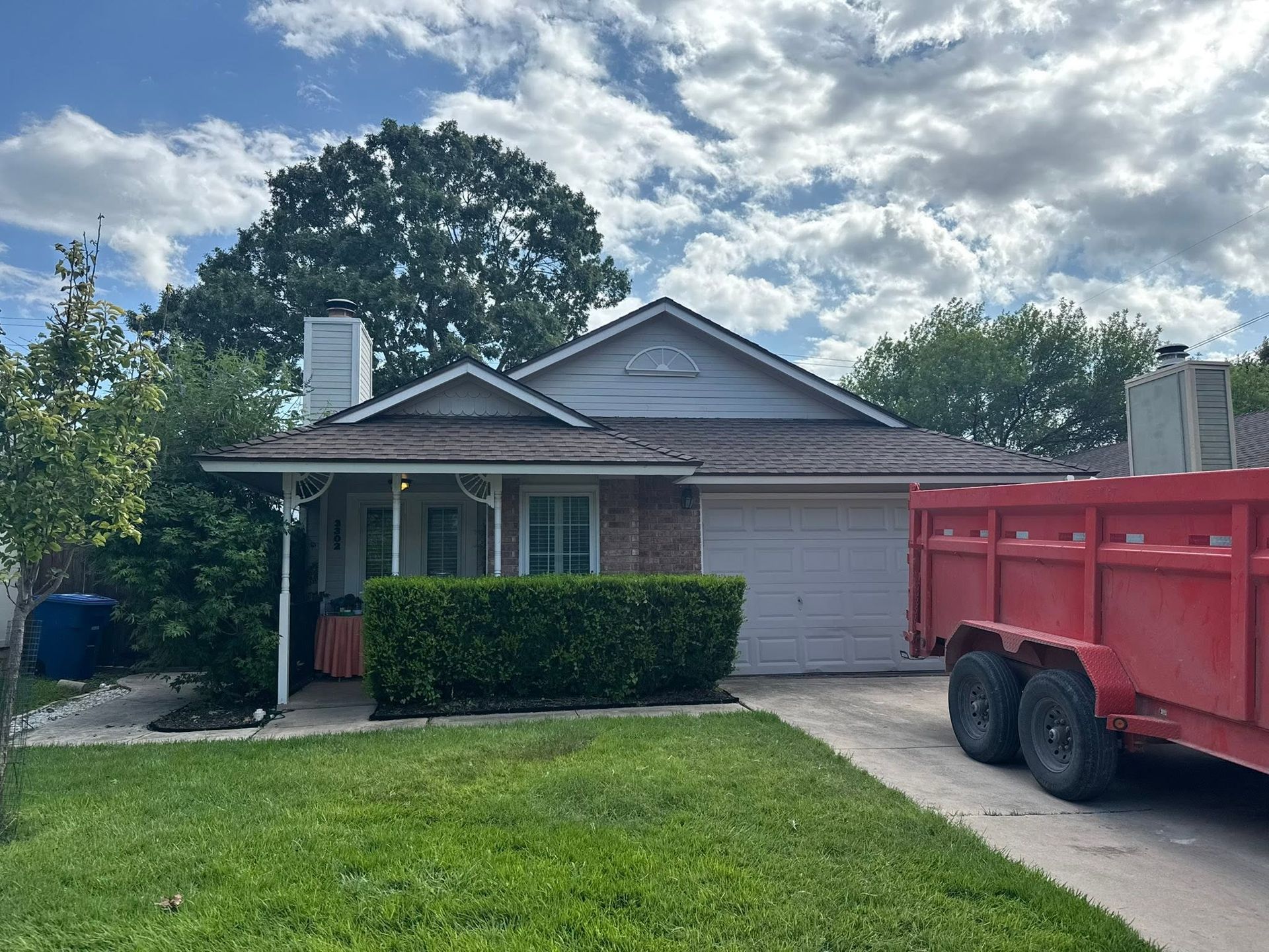 Suburban house with a front lawn, driveway, and red dump trailer under a cloudy sky