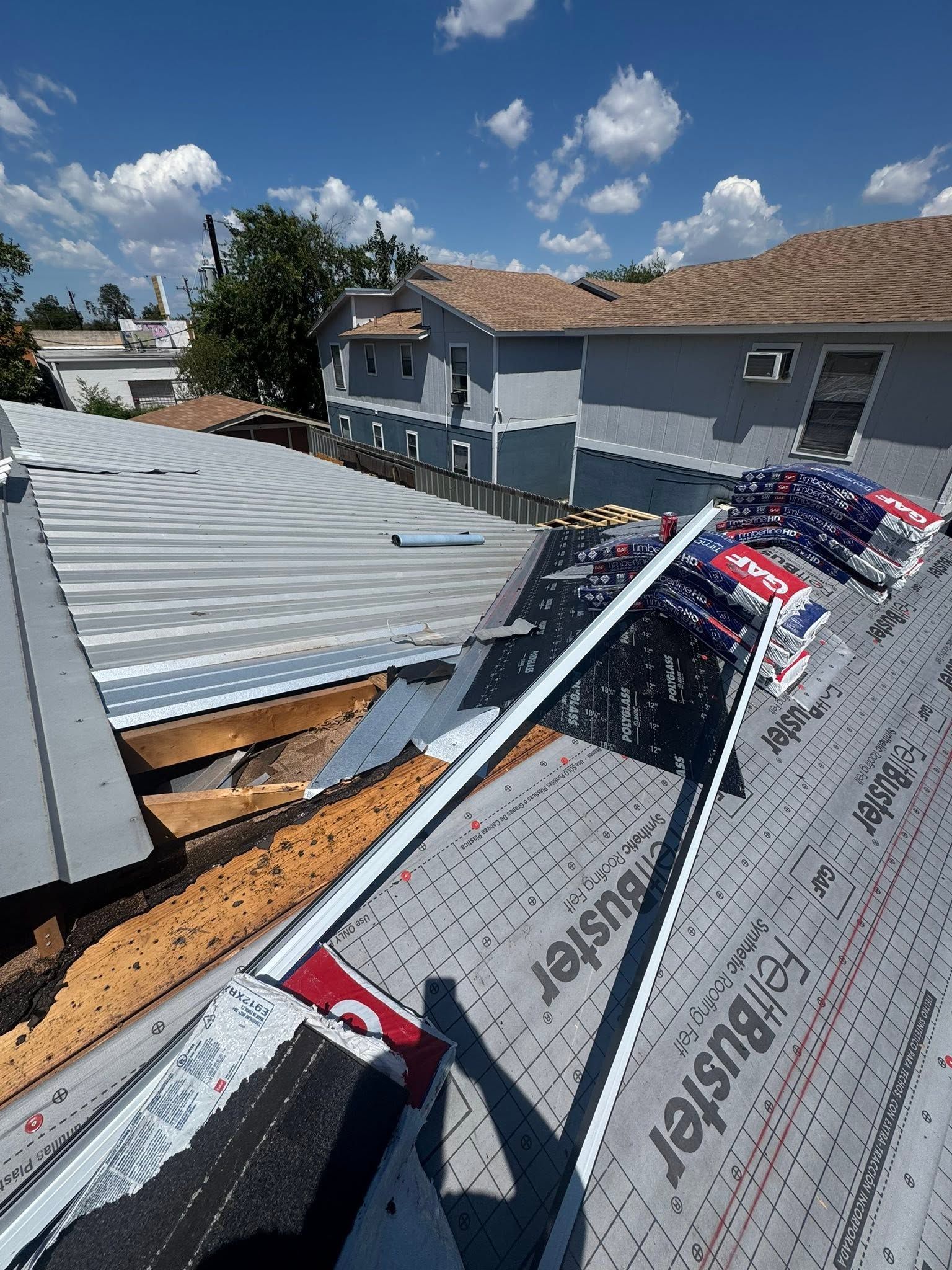 Roof under construction with exposed plywood, metal panels, and protective underlayment on a sunny day