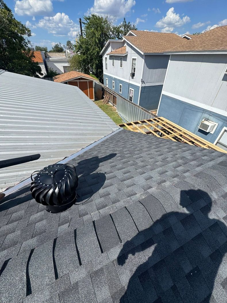 Rooftop view of shingles, a black bag, and a person’s shadow overlooking neighboring houses.
