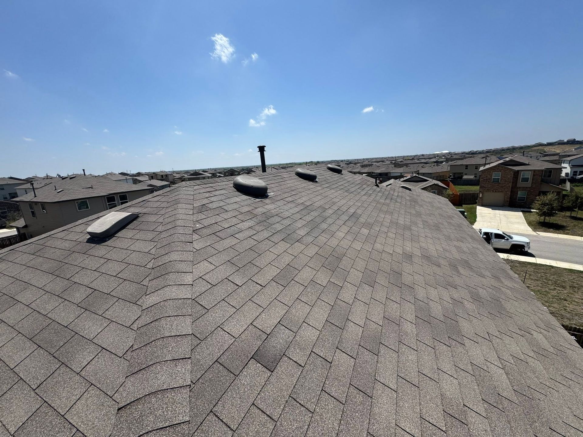 Gray shingled roof under a clear blue sky, seen from above with a vent pipe centered.