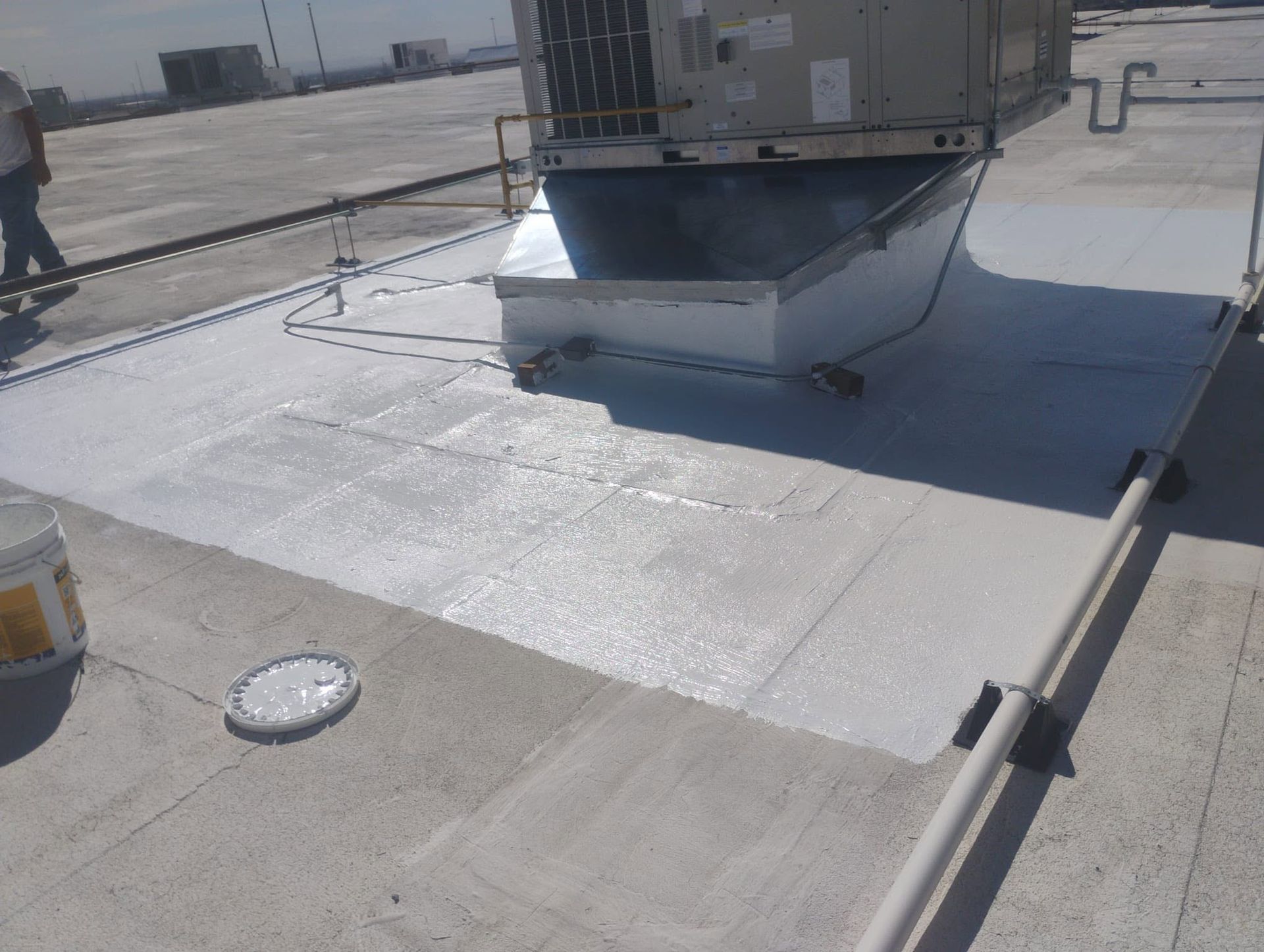 Rooftop with HVAC unit, white waterproof membrane, and a person working near the edge