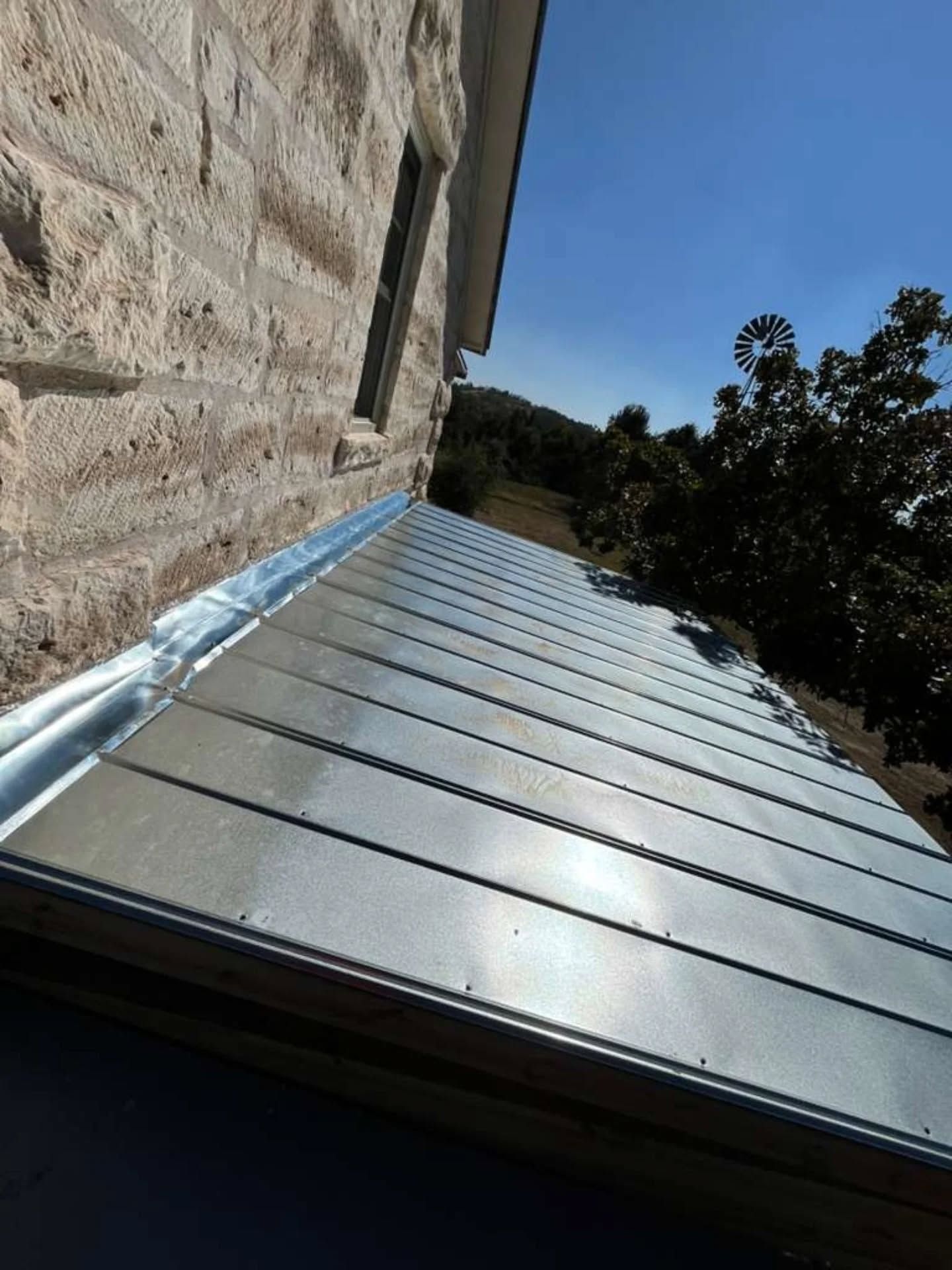 Metal roof beside a stone wall, viewed from below on a sunny day